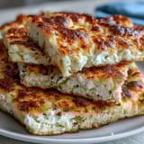 Golden-brown Fluffy Cottage Cheese Flatbread bubbling in a skillet, surrounded by fresh herbs, ready for wraps or dipping.