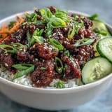 Freshly cooked spicy Easy Korean Beef Bowl with ground beef glazed in gochujang sauce, topped with crisp cucumber, carrots, and sesame seeds, served over steamed rice.
