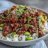 A vibrant Korean ground beef bowl with spicy gochujang beef, fresh cucumber, carrots, kimchi, and sesame seeds over steamed rice.