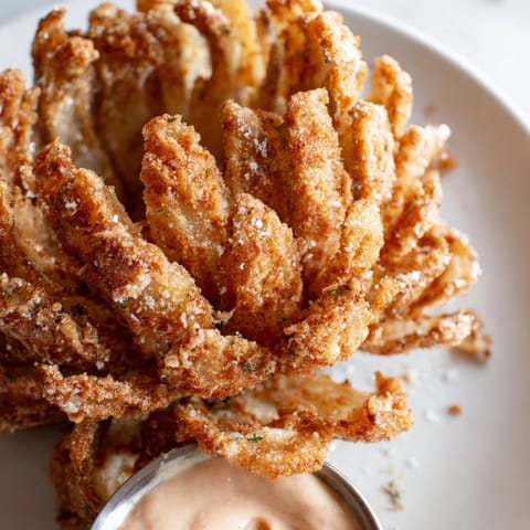 Image of a freshly fried Blooming Onion, perfect appetizer, served with a zesty, chilled dipping sauce.