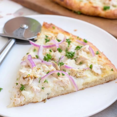 Golden, bubbly Chicken Alfredo Pizza slices rest on a wooden cutting board with melted mozzarella and a parsley garnish.