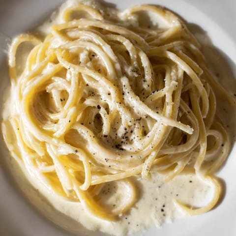 Close-up of Spaghetti Cacio e Pepe topped with freshly grated Pecorino Romano, a rustic wooden fork twirling pasta in golden light.  