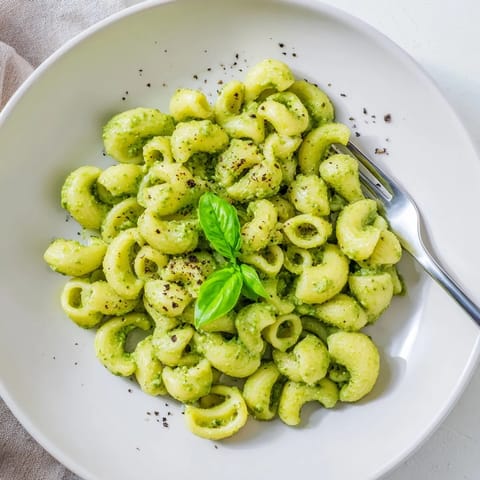 Creamy Avocado Pesto Mac served warm in a rustic bowl, garnished with fresh basil leaves and grated Parmesan cheese.  