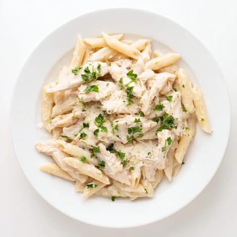 Golden-brown roasted garlic chicken penne pasta coated in a rich, velvety cream sauce with fresh parsley garnish.
