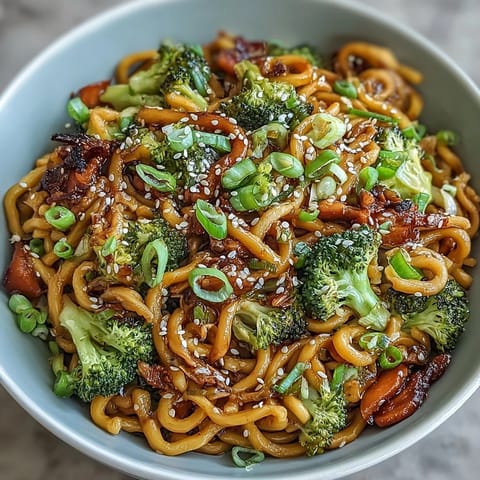Vibrant Asian teriyaki noodle bowl featuring colorful carrots, broccoli, and sesame seeds over glossy noodles.