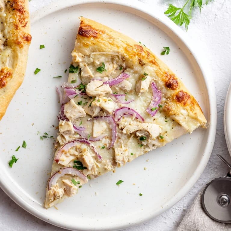 Sliced Chicken Alfredo Pizza shows creamy Alfredo sauce, tender chicken, and red onion on a crisp golden crust.