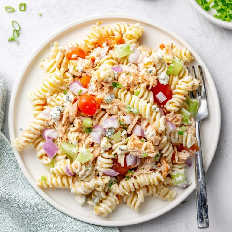 Buffalo Chicken Pasta Salad in a serving bowl, garnished with fresh chives and halved cherry tomatoes on a rustic table.