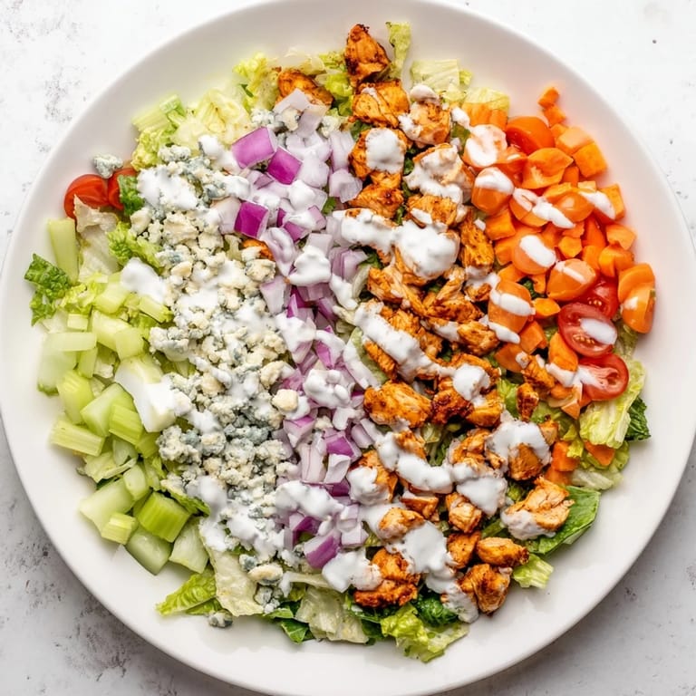 A close-up view of Buffalo Chicken Chopped Salad highlights juicy, sauced chicken pieces and bright red cherry tomatoes.