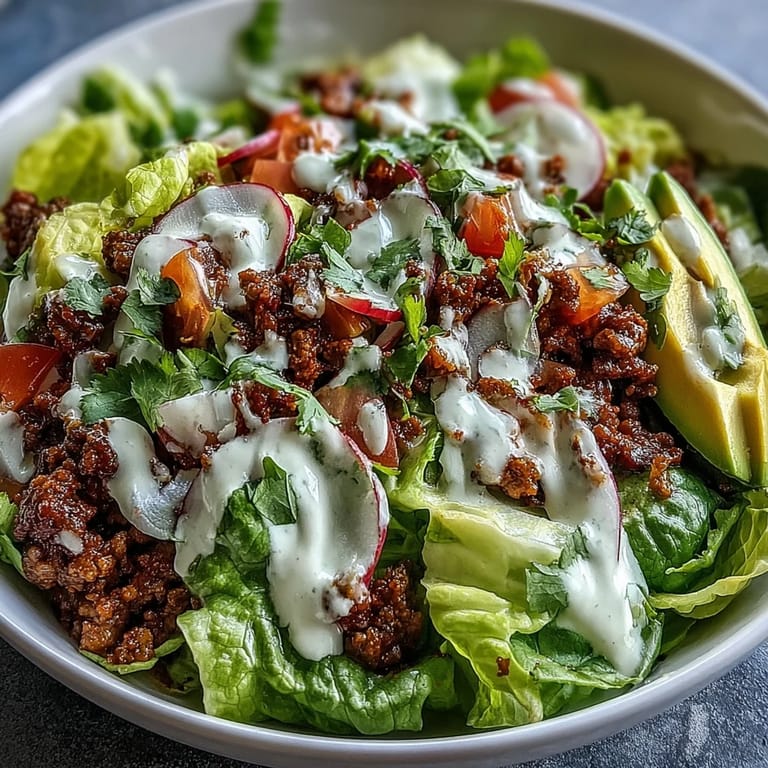 Vibrant taco bowl featuring lean ground beef, fresh vegetables, and creamy lime yogurt dressing in a gluten-free meal.  