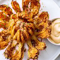 Golden-brown, crispy Blooming Onion with petals ready to dip in creamy sauce for sharing.
