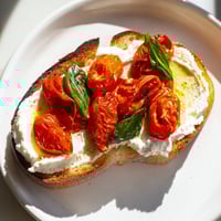 Golden-brown sourdough toast spread with creamy whipped ricotta and topped with juicy, slow-roasted cherry tomatoes and fresh basil.