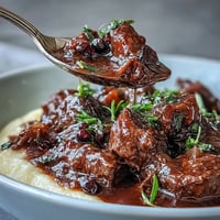 Creamy polenta topped with rich Venison Stew with Sloe Gin, featuring tender meat in a dark, glossy sauce.